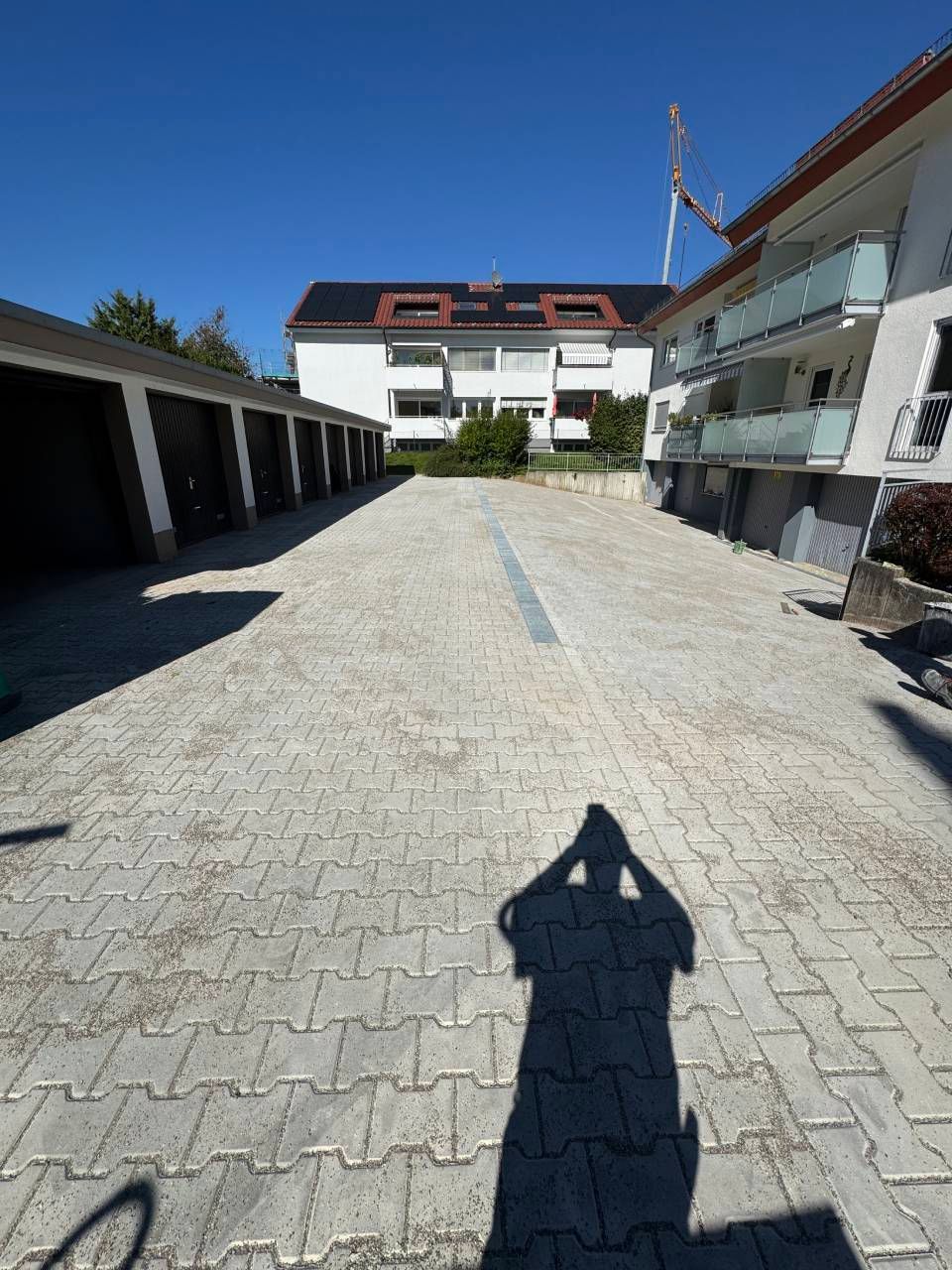 Sonniger Innenhof mit weißen Gebäuden und einem gepflasterten Gehweg, Schatten des Fotografen im Vordergrund