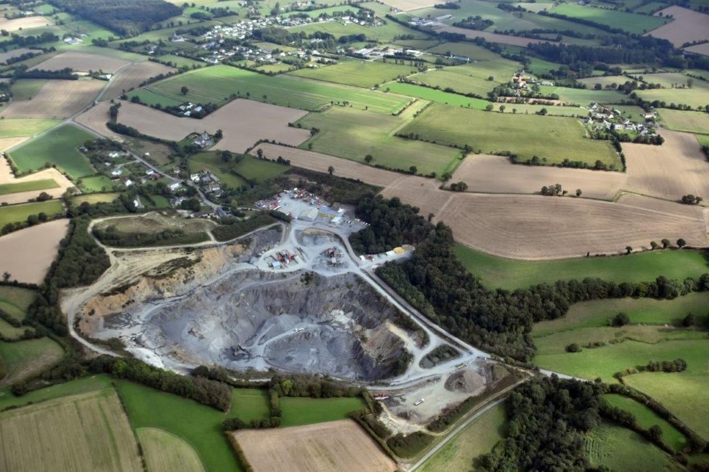 Vue aérienne d'une carrière entourée de terres agricoles et d'une petite ville dans un paysage rural.