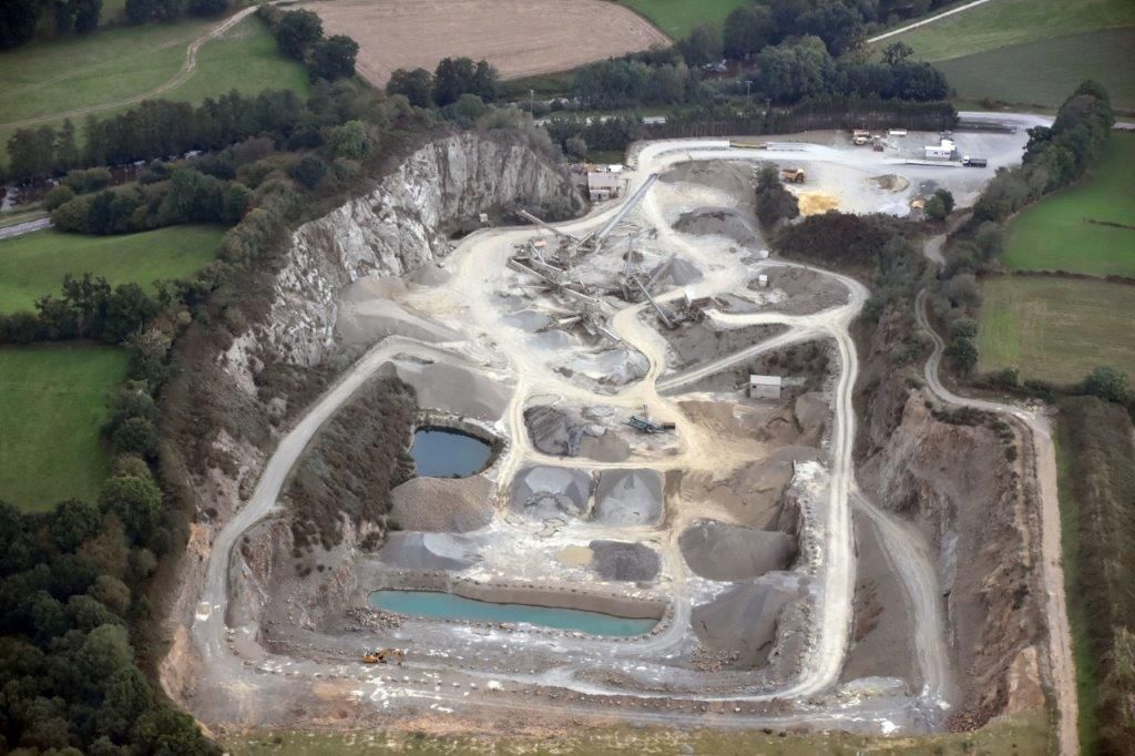 Vue aérienne d'une carrière : grande fosse à ciel ouvert à plusieurs niveaux, tas de gravier et petites mares d'eau.