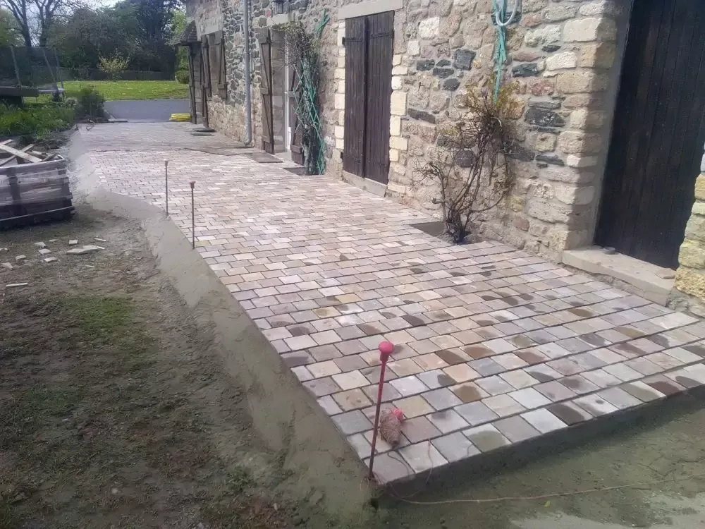 Patio en pierre avec rampe menant à un bâtiment avec portes en bois et murs en pierre.