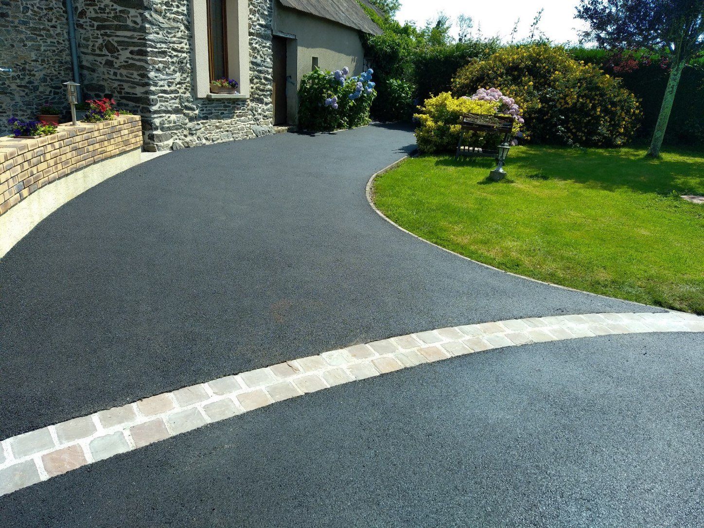 Allée de maison goudronnée et pavée bordée par de la pelouse.