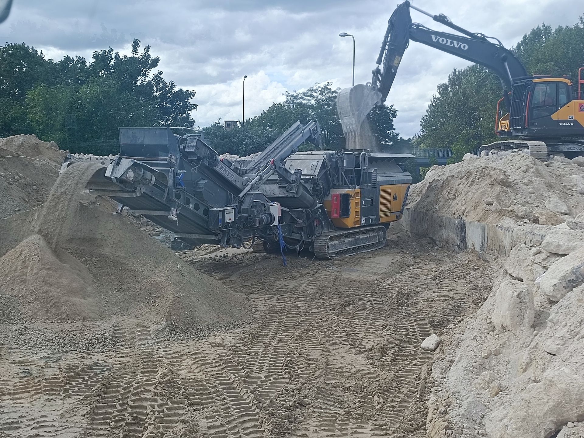 Une excavatrice déverse des gravats dans une machine de concassage sur un chantier de construction.