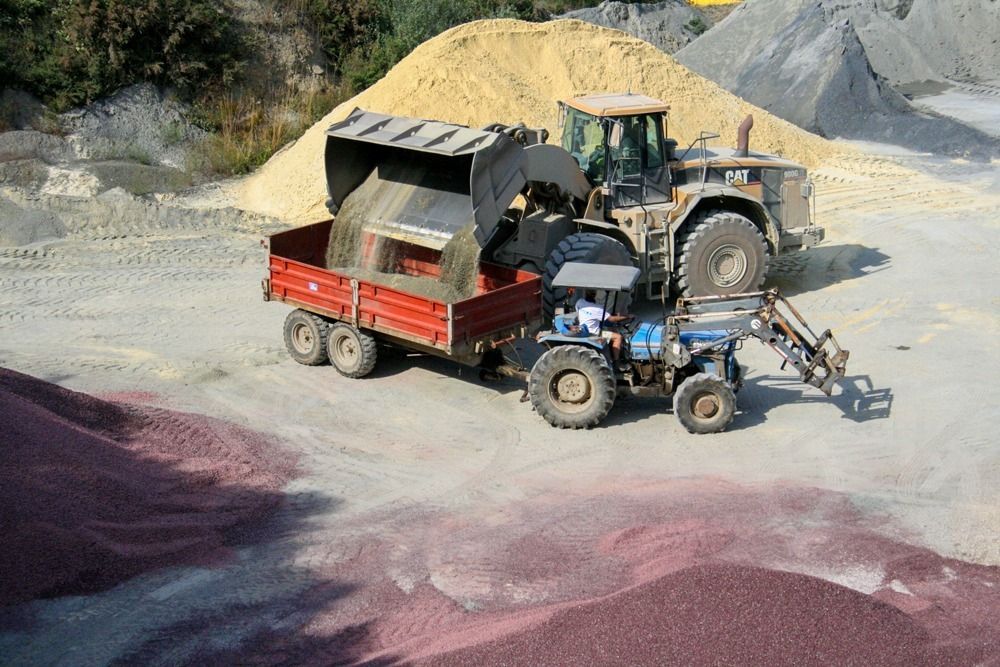Chargement de matériaux concassés dans une benne tractée par un tracteur.