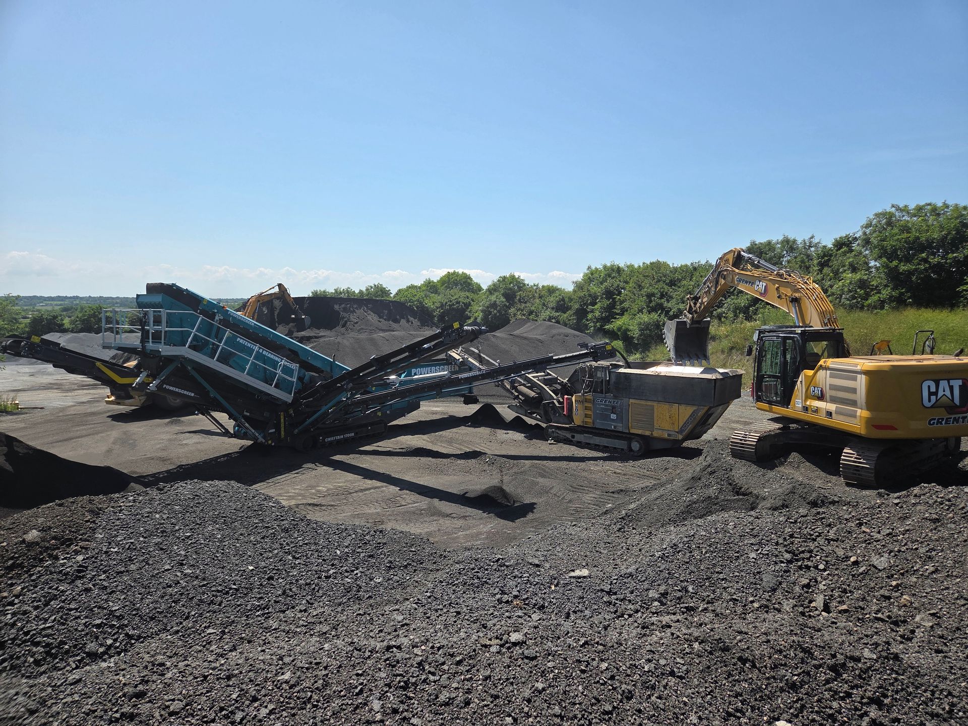 Une excavatrice charge des matériaux sombres dans un concasseur de pierres.