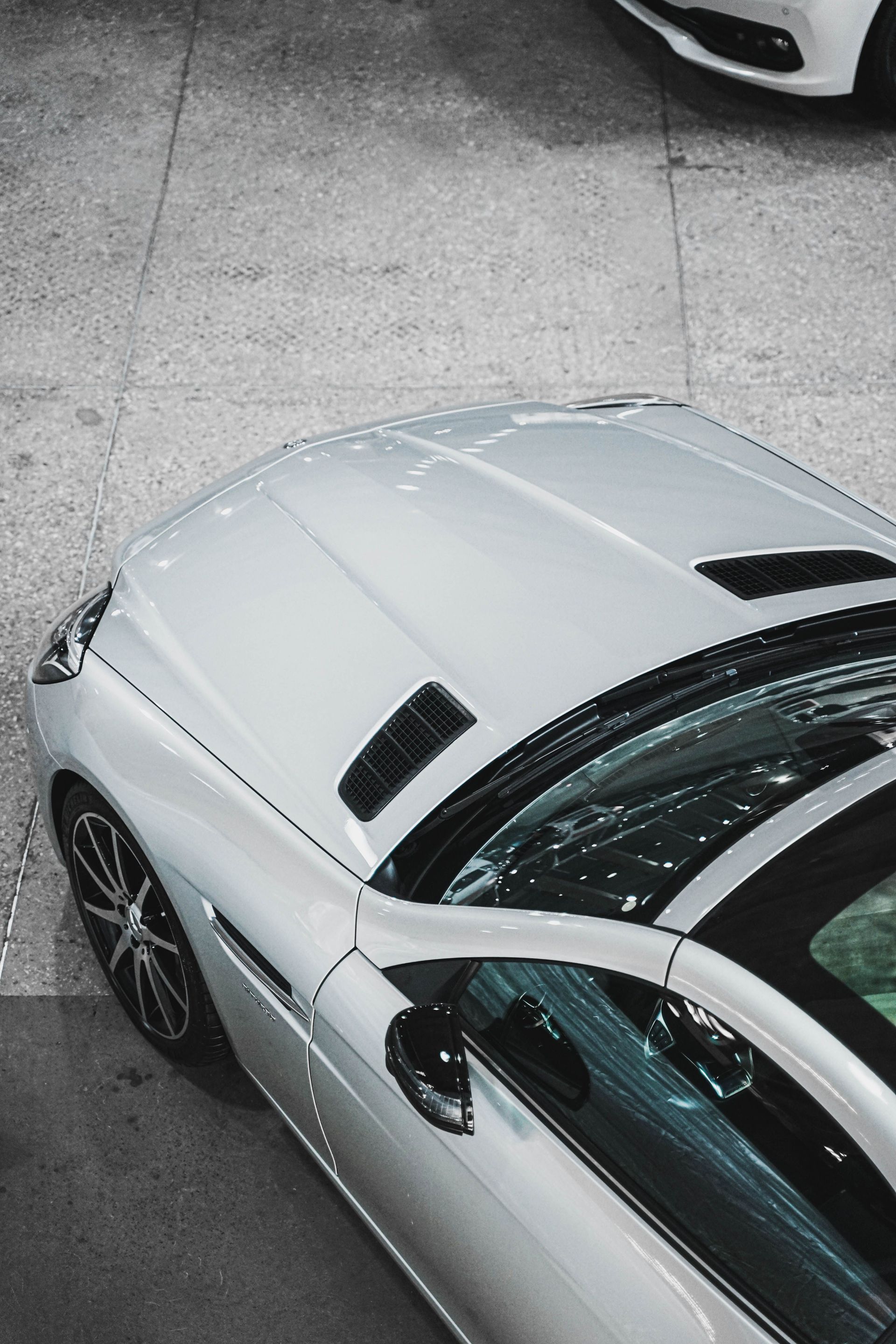 Voiture blanche vue du dessus sur un parking, avec un autre véhicule blanc partiellement visible à proximité