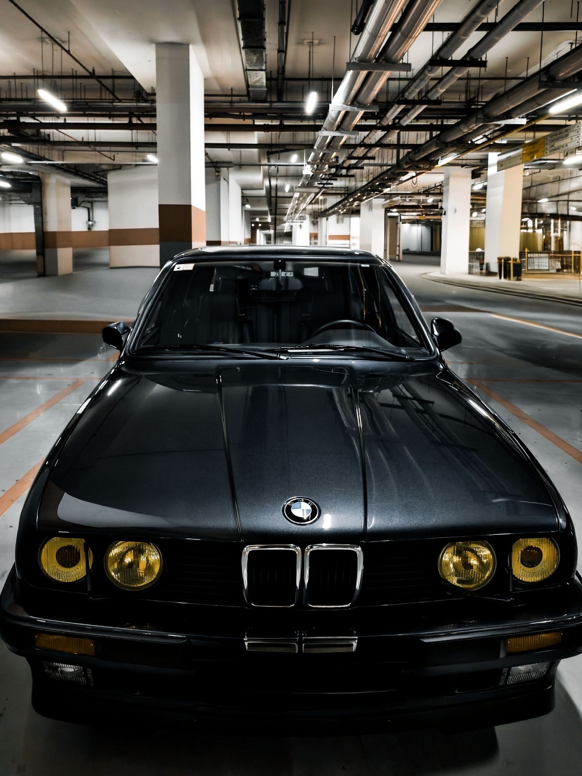 Berline BMW noire garée dans un parking souterrain, vue de face, phares allumés.