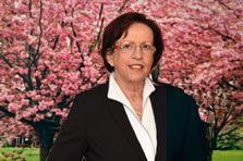 Eine Frau im Anzug und mit Brille steht vor einem Kirschblütenbaum.