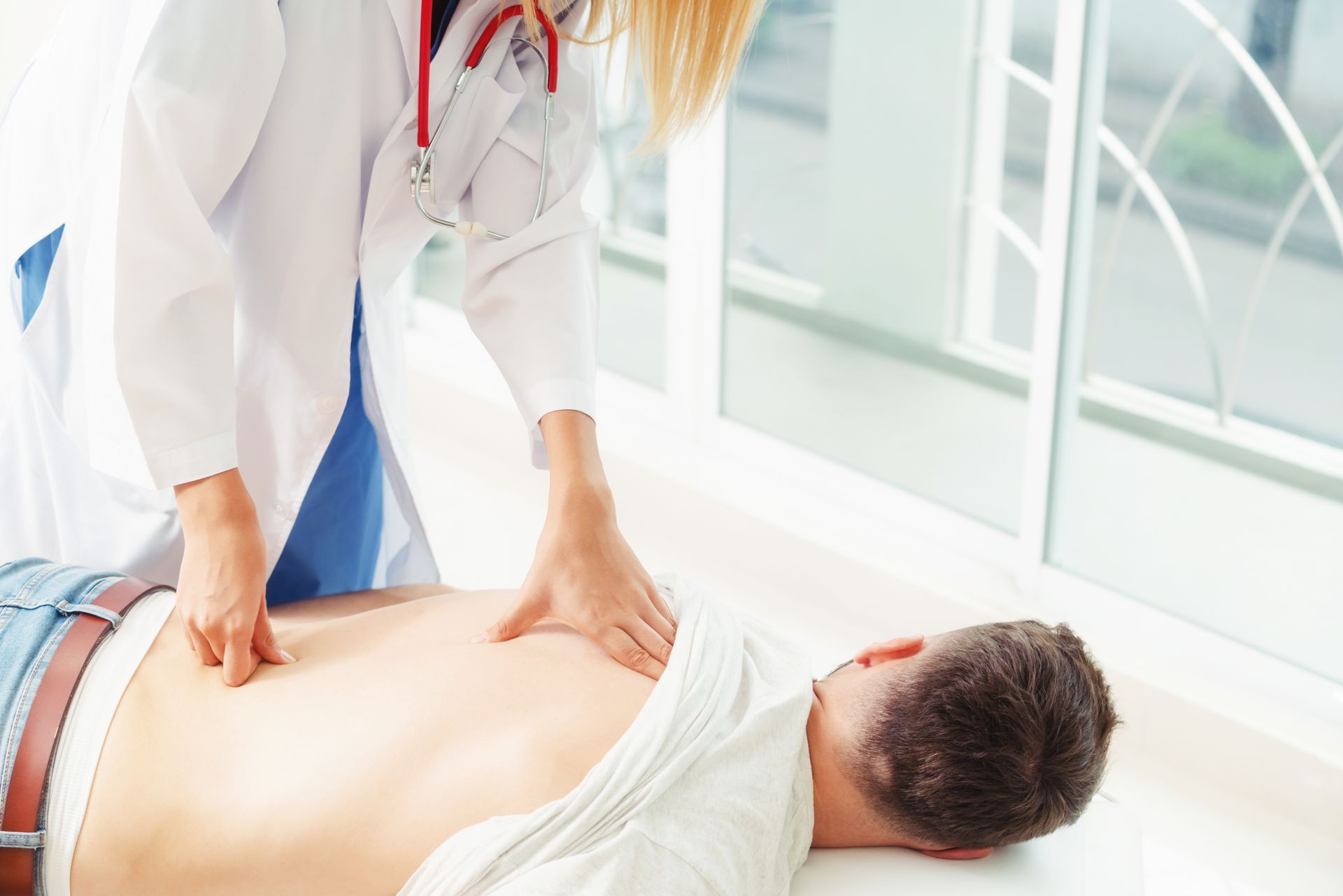 Ein Arzt führt in einer Klinik eine körperliche Untersuchung des Rückens einer Person durch.