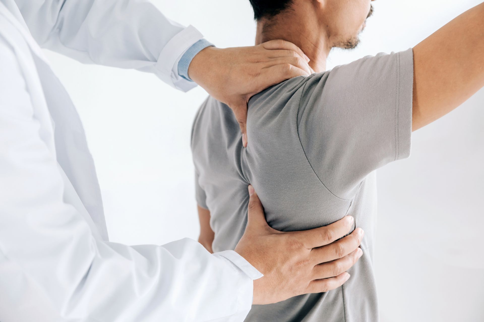 Ein Arzt im weissen Kittel führt eine körperliche Untersuchung des Rückens eines Patienten durch.
