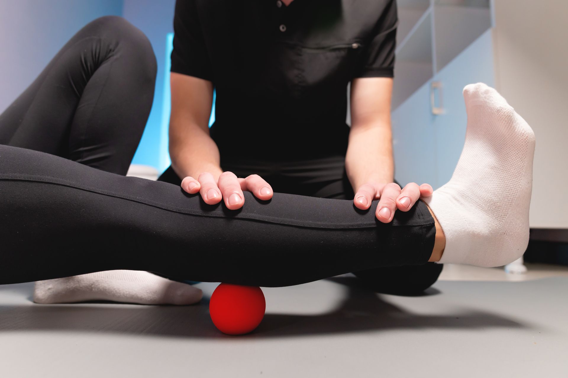 Ein Therapeut verwendet einen roten Ball, um eine myofasziale Entspannungstechnik an der Wadenmuskulatur eines Patienten durchzuführen.