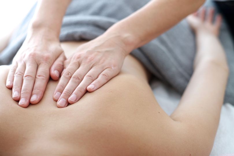 Eine Person liegt entspannt mit geschlossenen Augen auf dem Bauch und geniesst eine Schultermassage in einem Spa-Ambiente mit Rosenblättern.