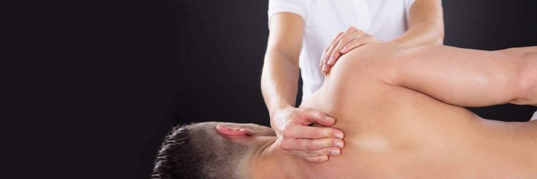 Eine Person erhält vor dunklem Hintergrund eine Schulter- und Nackenmassage von einem Therapeuten.