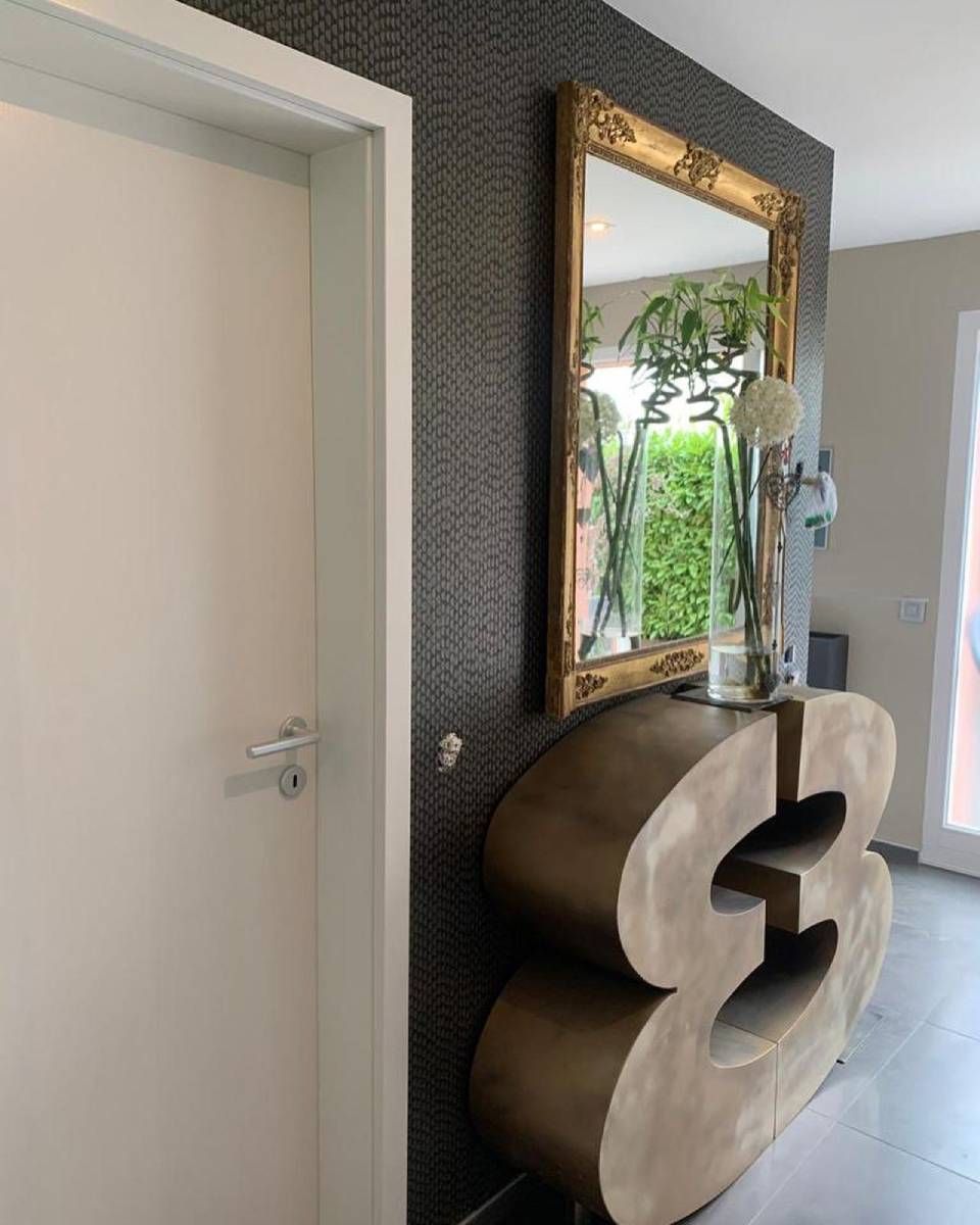 Une console dorée en forme de chiffre trois est placée contre un mur sombre à la texture travaillée.