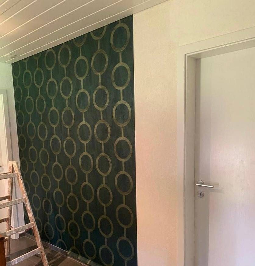 Un mur partiellement recouvert de papier peint vert foncé à motif géométrique circulaire doré répétitif.