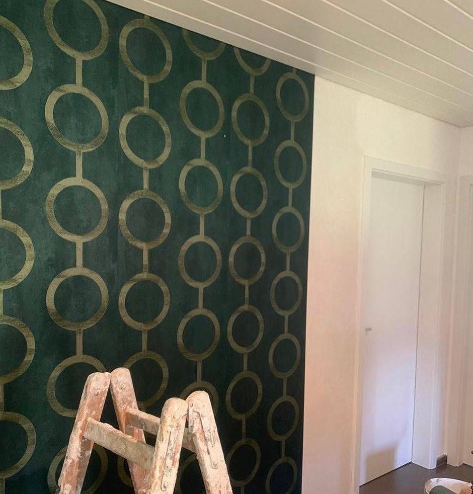 Un escabeau se dresse devant un mur recouvert d'un papier peint vert foncé orné d'un motif de cercles dorés répétitif.