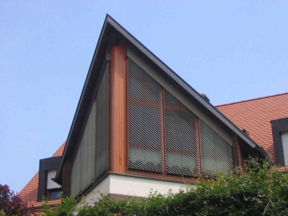 Dreieckige Gebäudefassade mit Gitterwerk und Kupferelementen vor blauem Himmel.