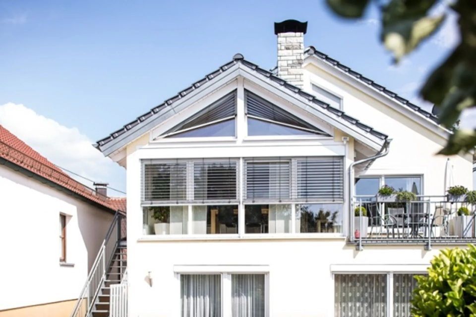 Weisses Haus mit dreieckigem Fenster über grossen Fenstern und einem kleinen Balkon.
