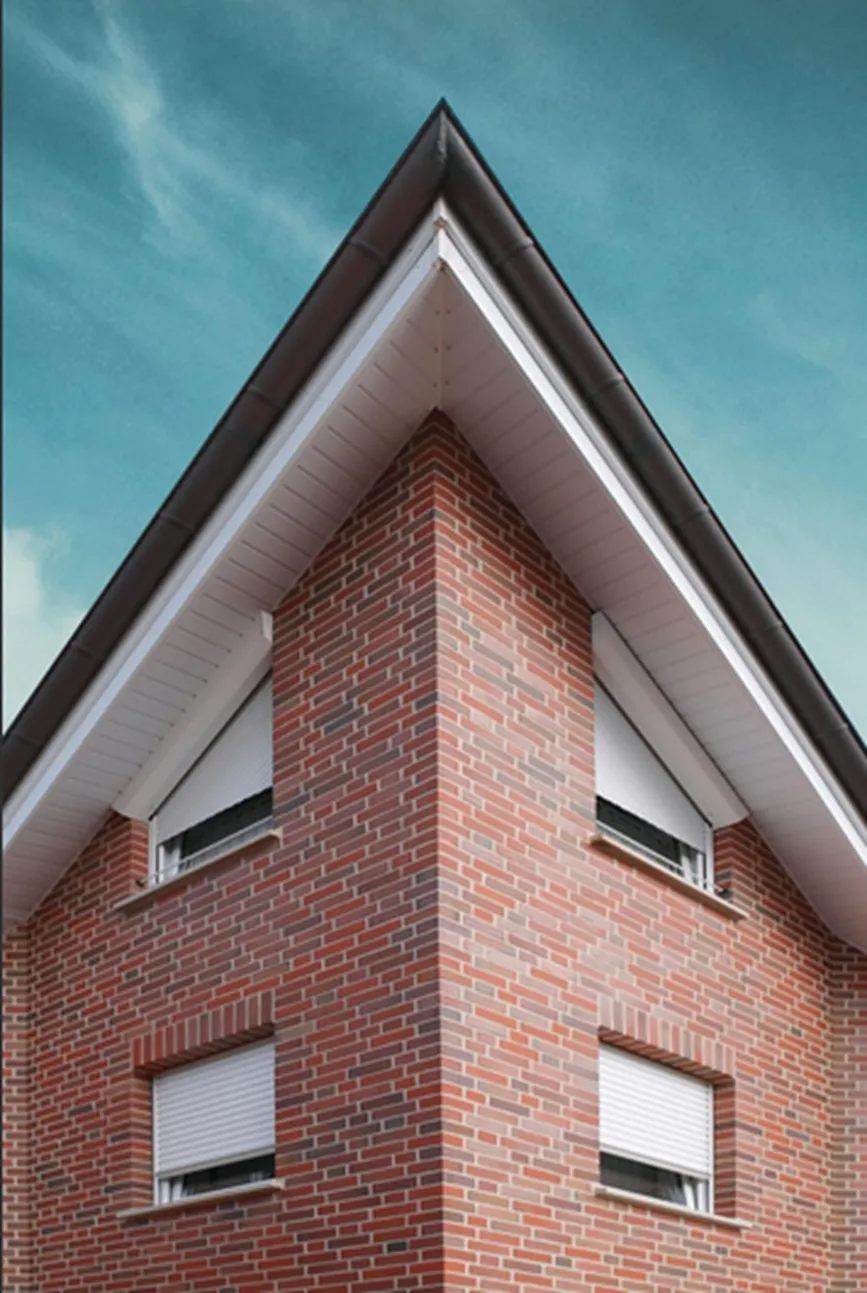 Eckgebäude aus Backstein mit dreieckigem Dach und weissen Fensterläden.