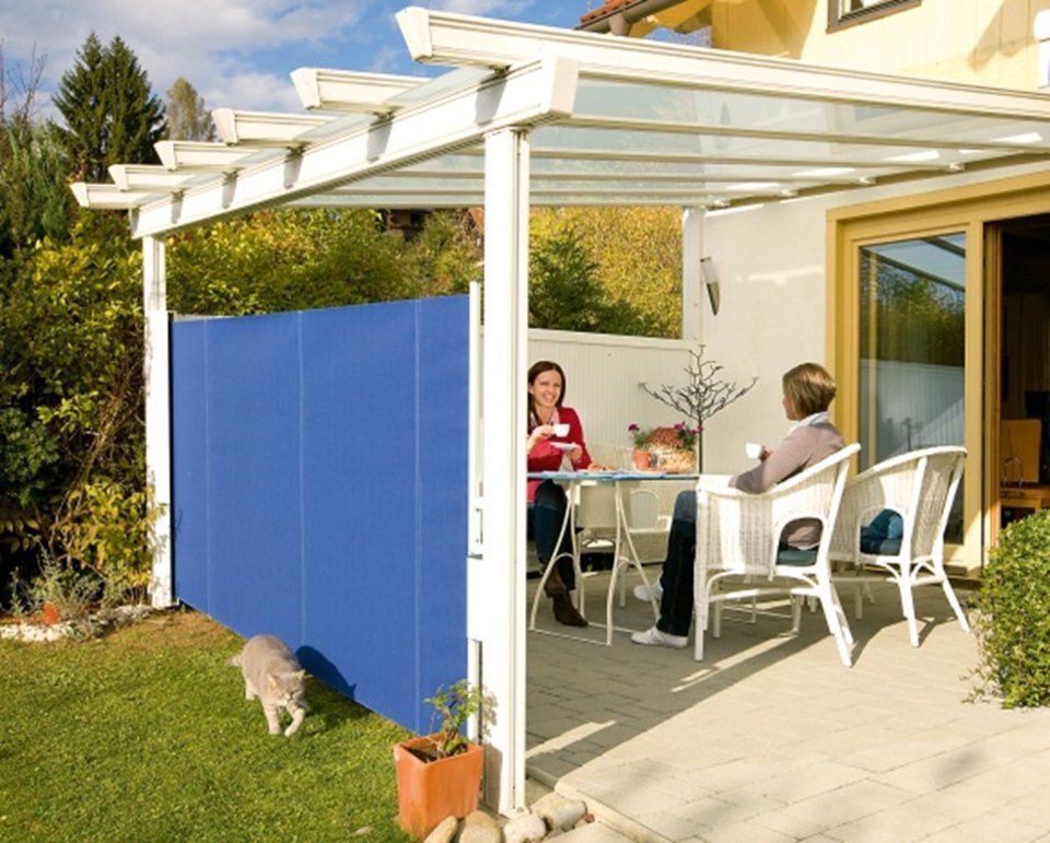 Zwei Frauen sitzen an einem Tisch auf einer Terrasse, die durch einen blauen Sichtschutz und eine Pergola abgetrennt ist.