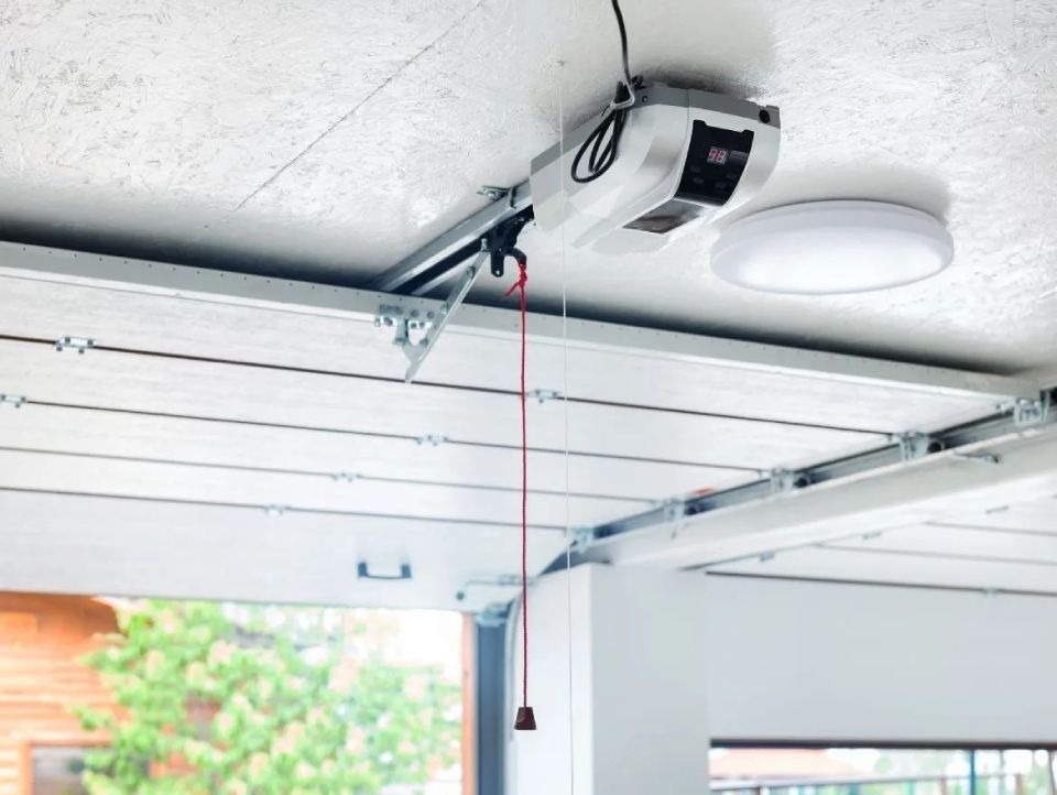 Garagentoröffner mit roter Notentriegelungsschnur, montiert an einer weissen Decke neben einer Lampe.