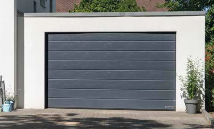 Ein hellblauer Lieferwagen parkt in einer Garage mit Blick auf ein Haus mit rotem Dach und dessen Hof.