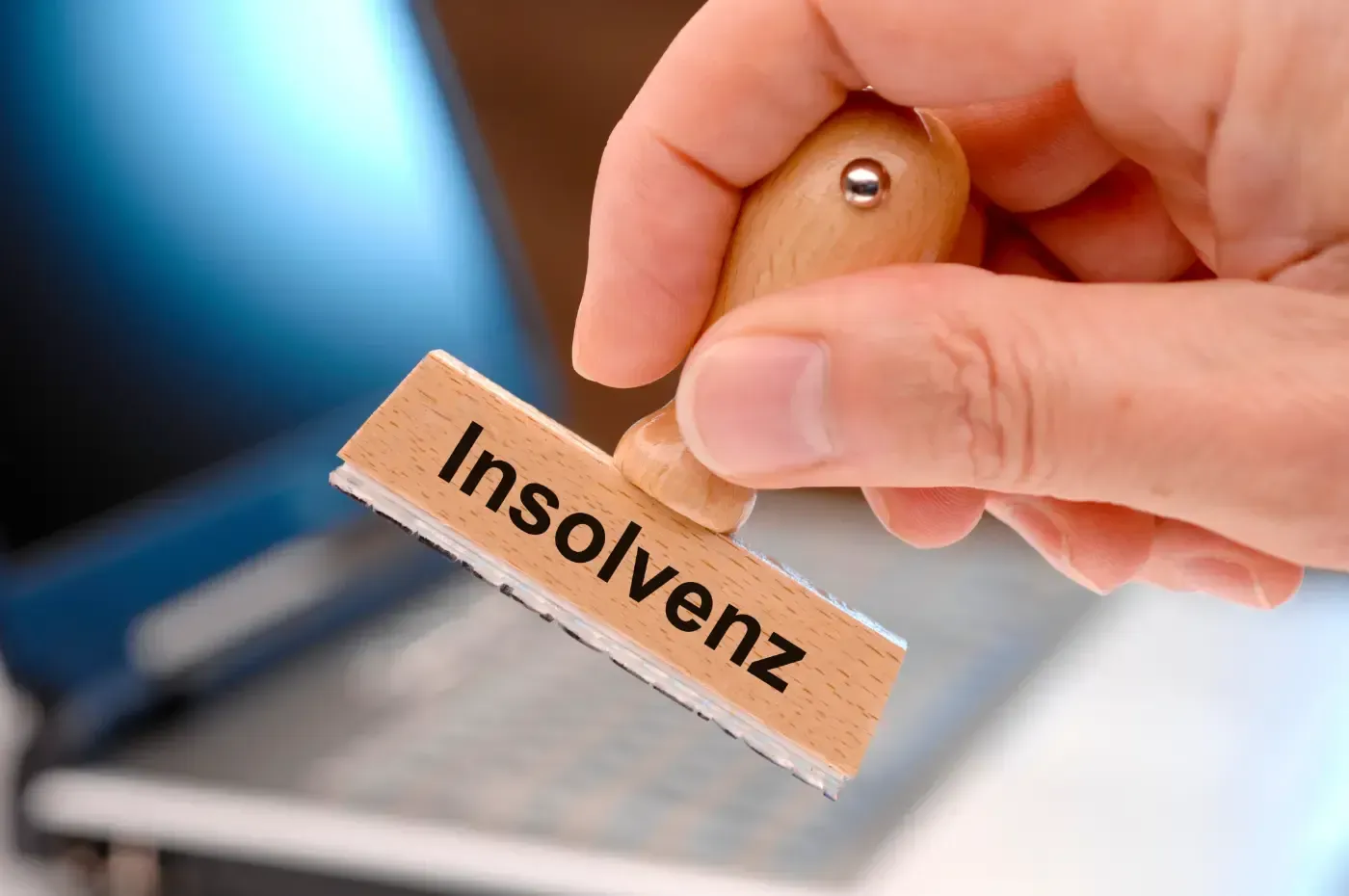 Eine Hand hält einen Stempel mit der Aufschrift „Insolvenz“ über einen Laptop.