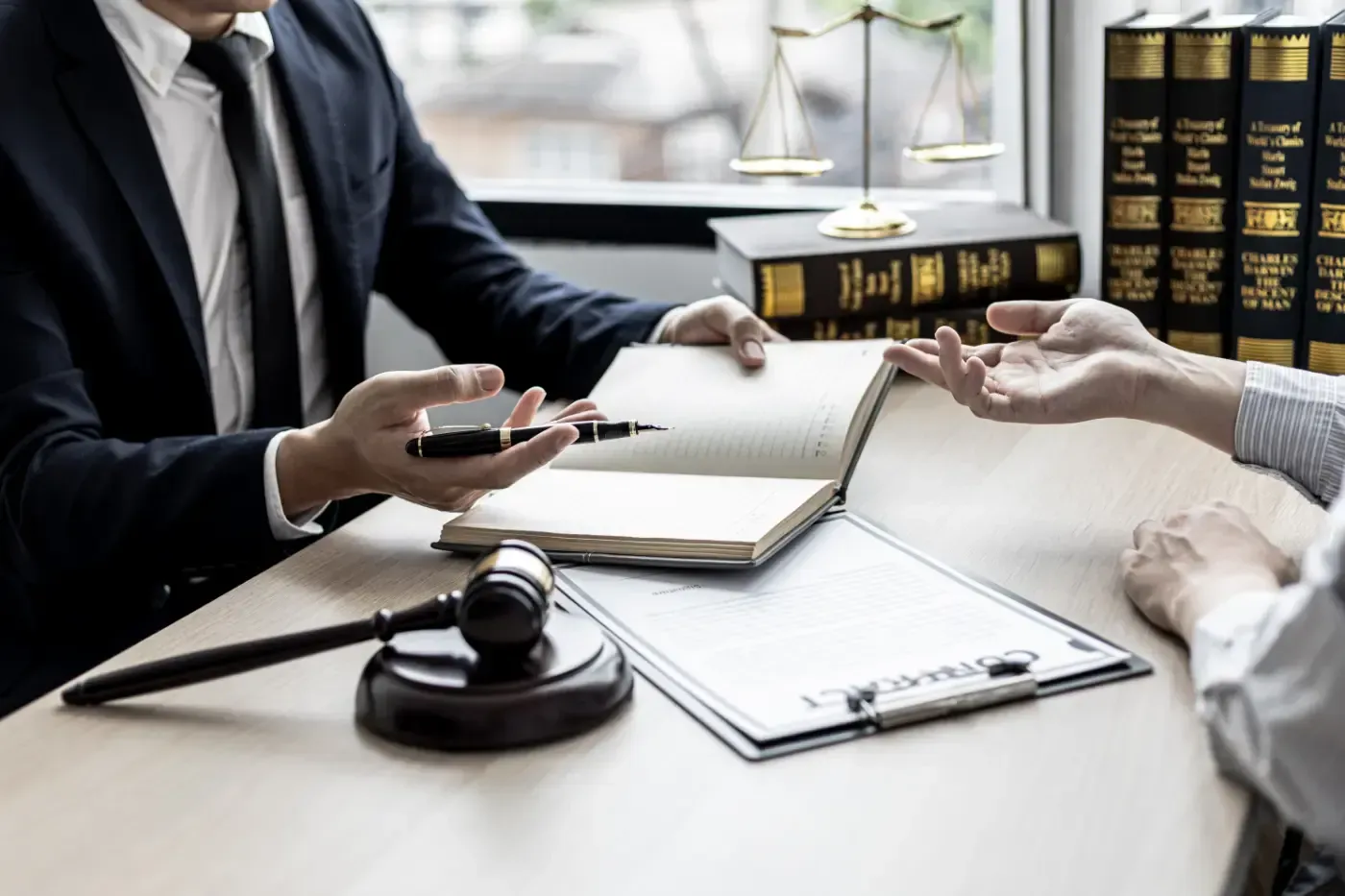 Anwalt und Mandant prüfen Dokumente an einem Schreibtisch; Hammer und Gesetzbücher liegen bereit.