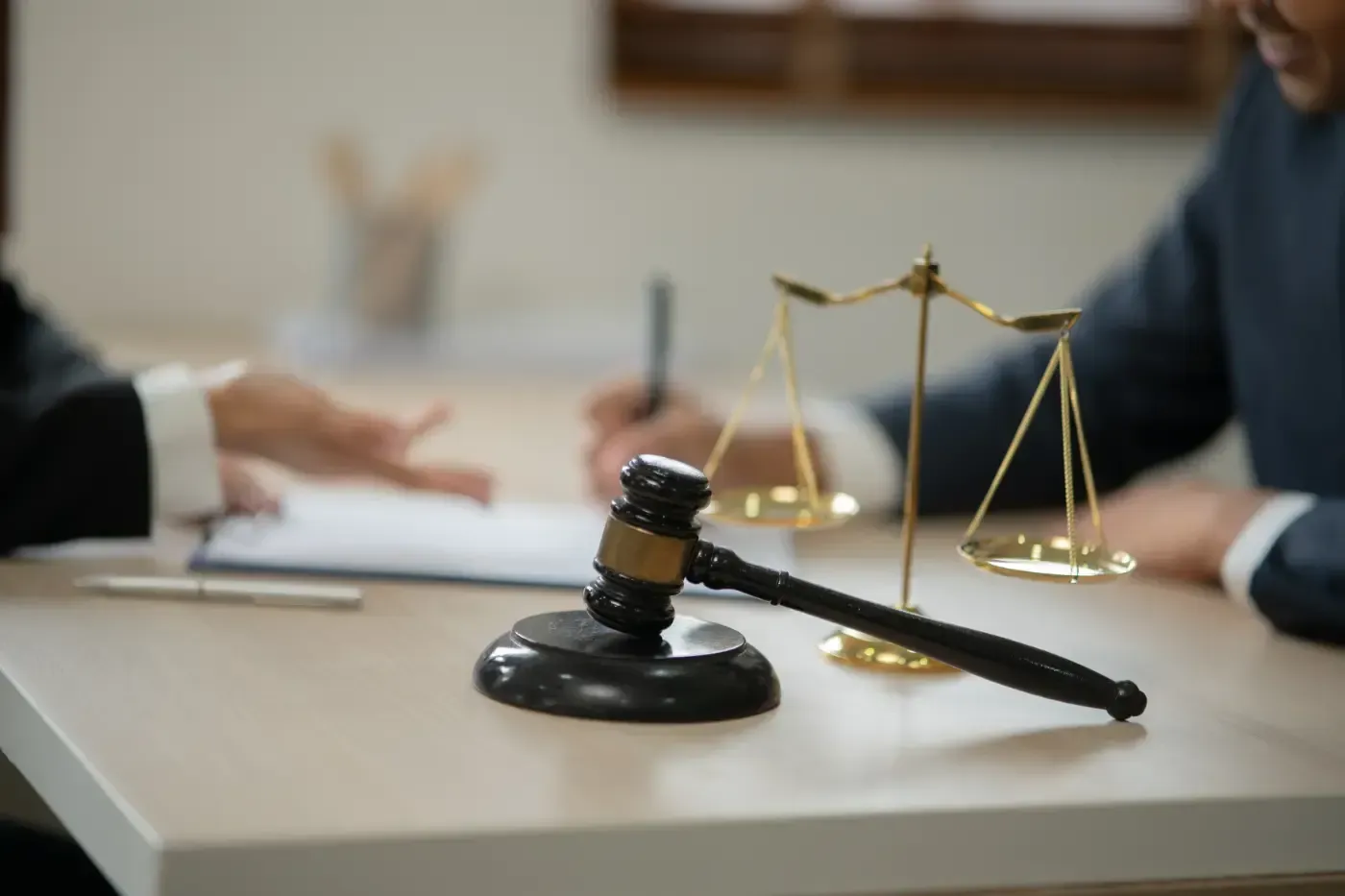 Hammer auf dem Tisch vor einer Waage und zwei Personen, von denen eine ein Dokument unterzeichnet.