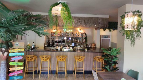 Un restaurante con barra, taburetes, mesas y palmeras.