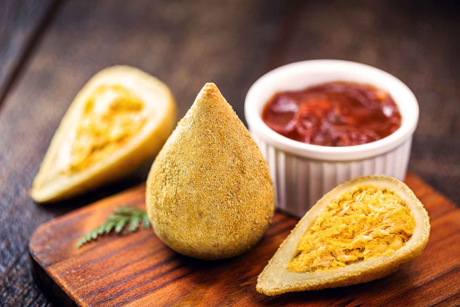 Una tabla de cortar de madera cubierta con comida frita y un tazón de salsa.
