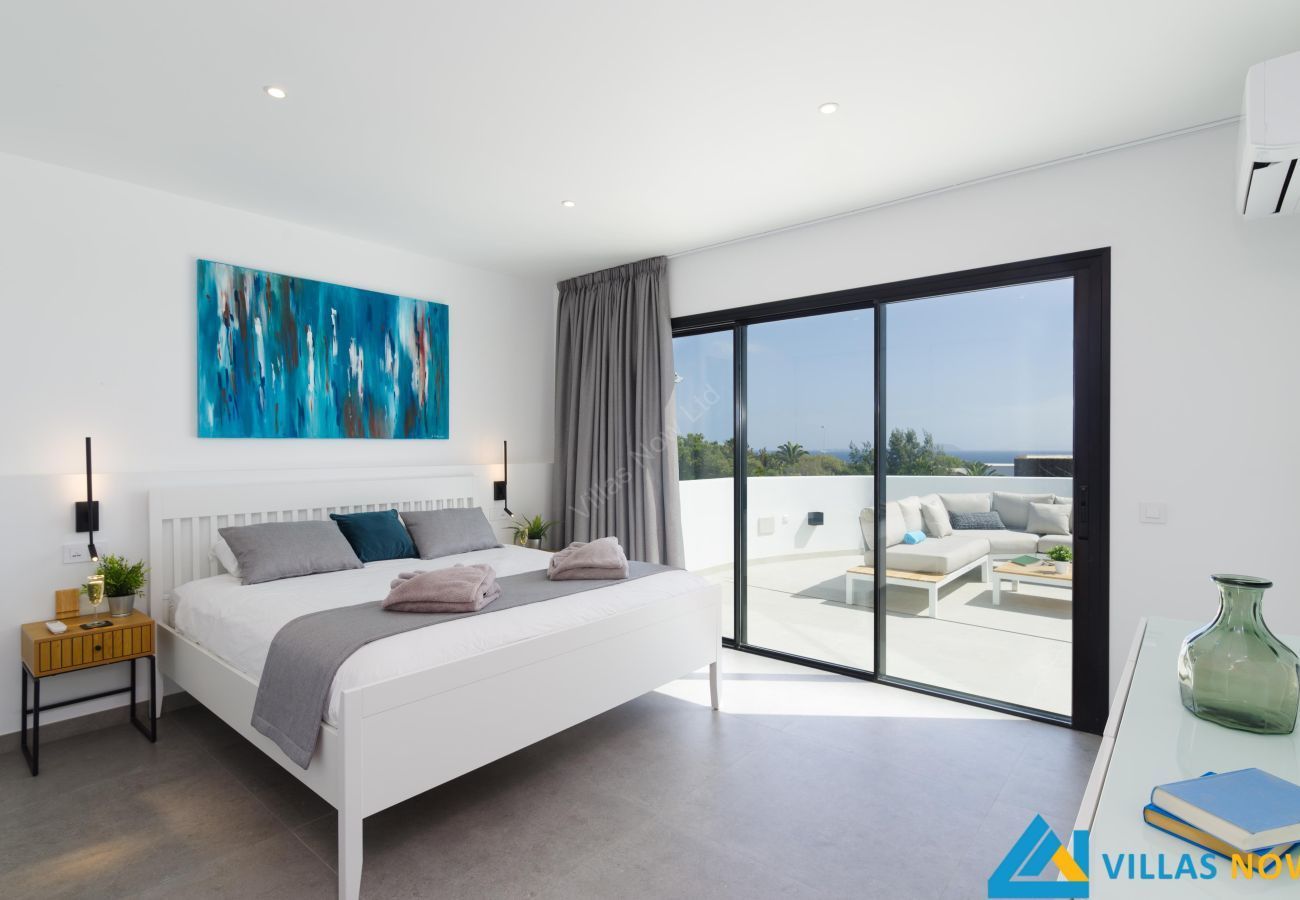 Bright modern bedroom with a bed, blue wall art, and sliding doors to a sunny balcony with lounge chairs