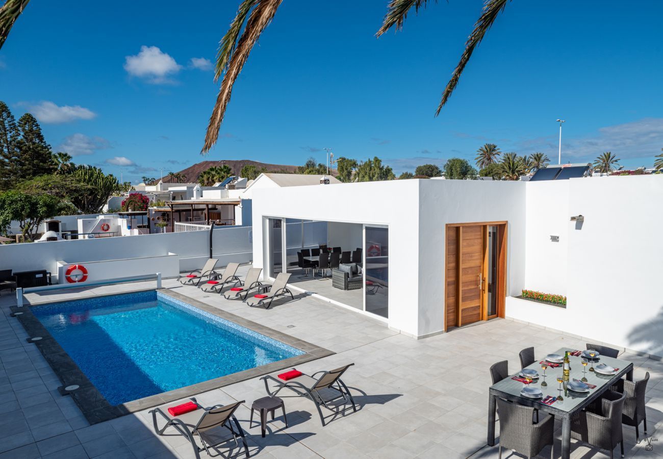Modern villa courtyard with a blue swimming pool, sun loungers, and outdoor dining area under a clear sky