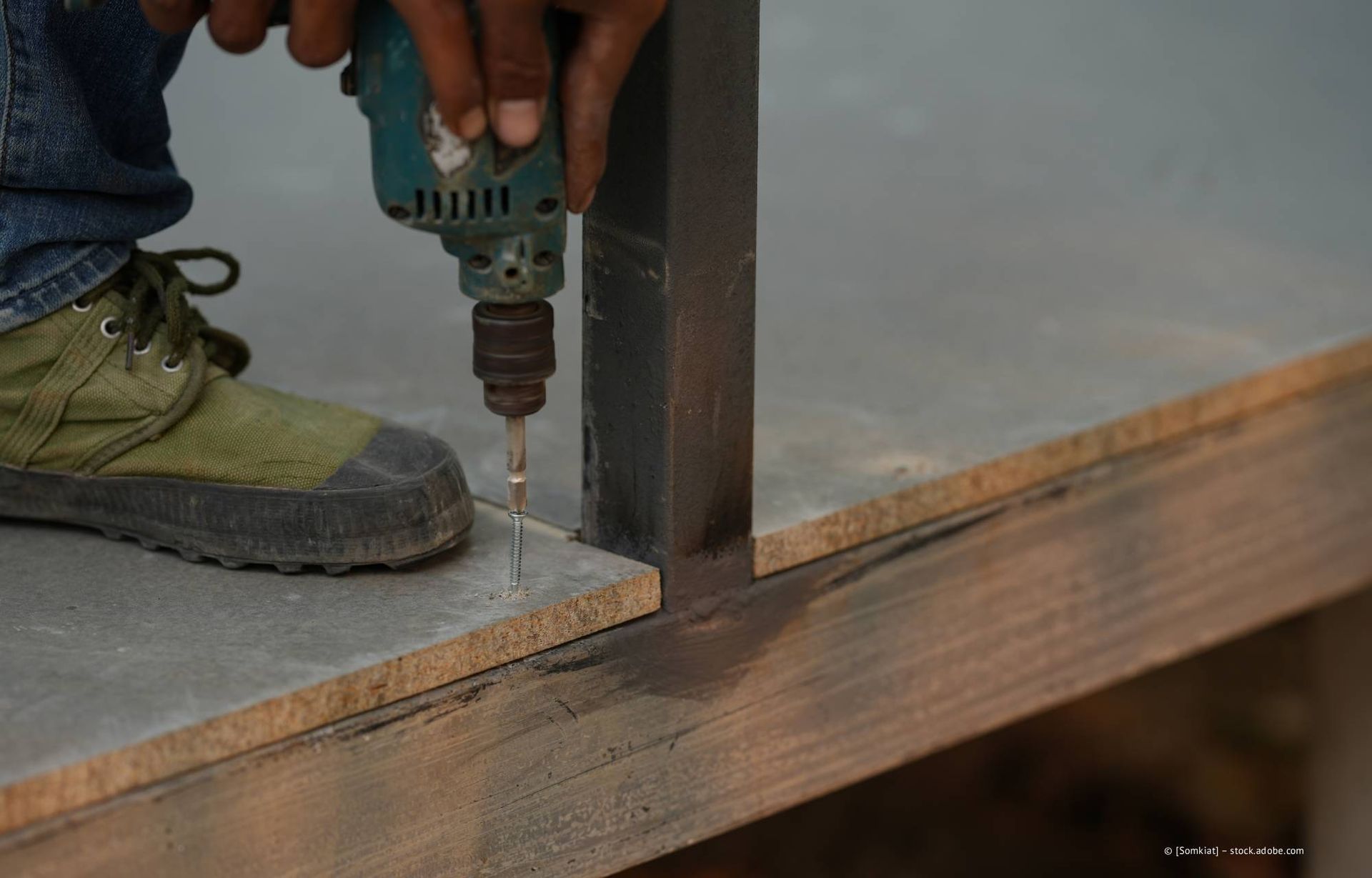 Eine Person bohrt im Freien mit einer Bohrmaschine in Holz.