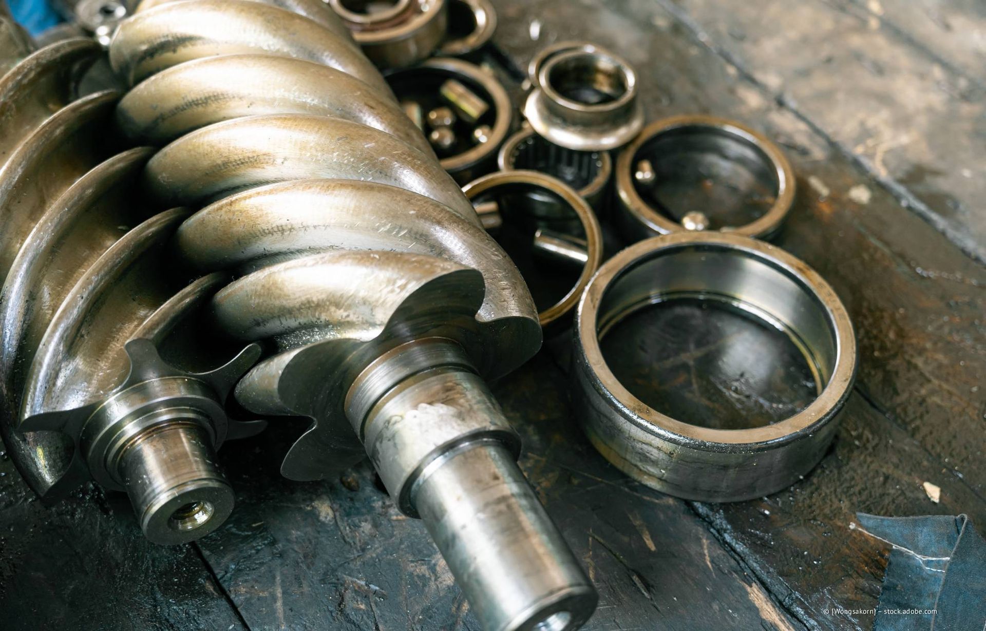 Nahaufnahme von zerlegten Teilen eines industriellen Luftkompressors, darunter ein Schraubenrotor und Lager.