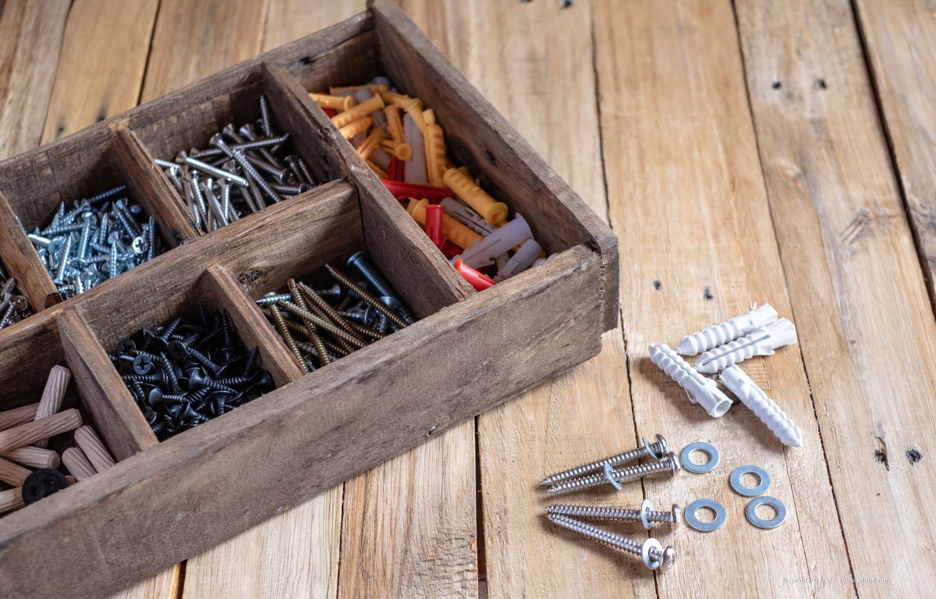 Werkzeugkasten aus Holz mit Schrauben und Dübeln auf einer Holzoberfläche.