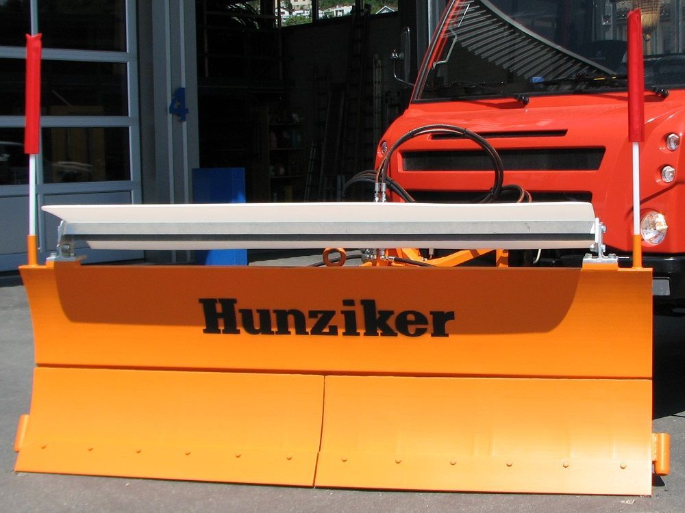 Orangefarbener Schneepflug mit „Hunziker“-Logo an einem orangefarbenen LKW. An den Enden stehen rote Leitstangen.