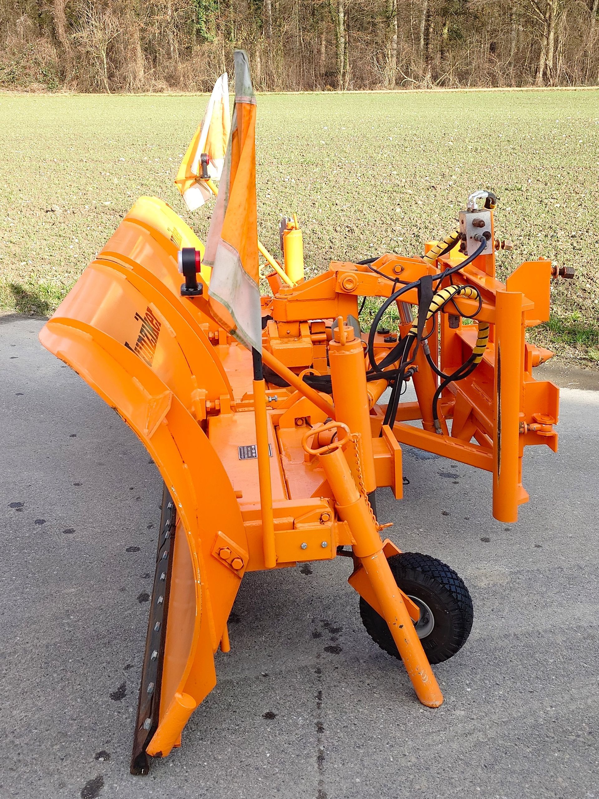 Orangefarbene Schneepflugmaschinen auf einer asphaltierten Fläche vor dem Hintergrund eines grünen Feldes.