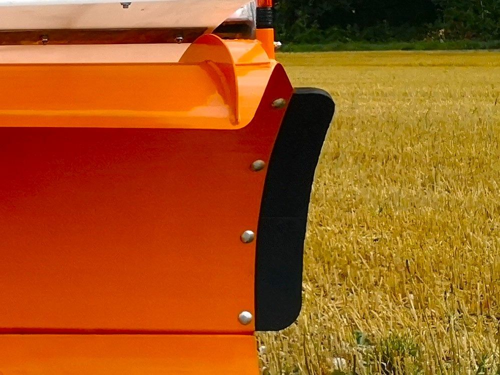 Orangefarbenes Detail einer landwirtschaftlichen Maschine mit einer schwarzen, gebogenen Seitenwand auf einem Feld.