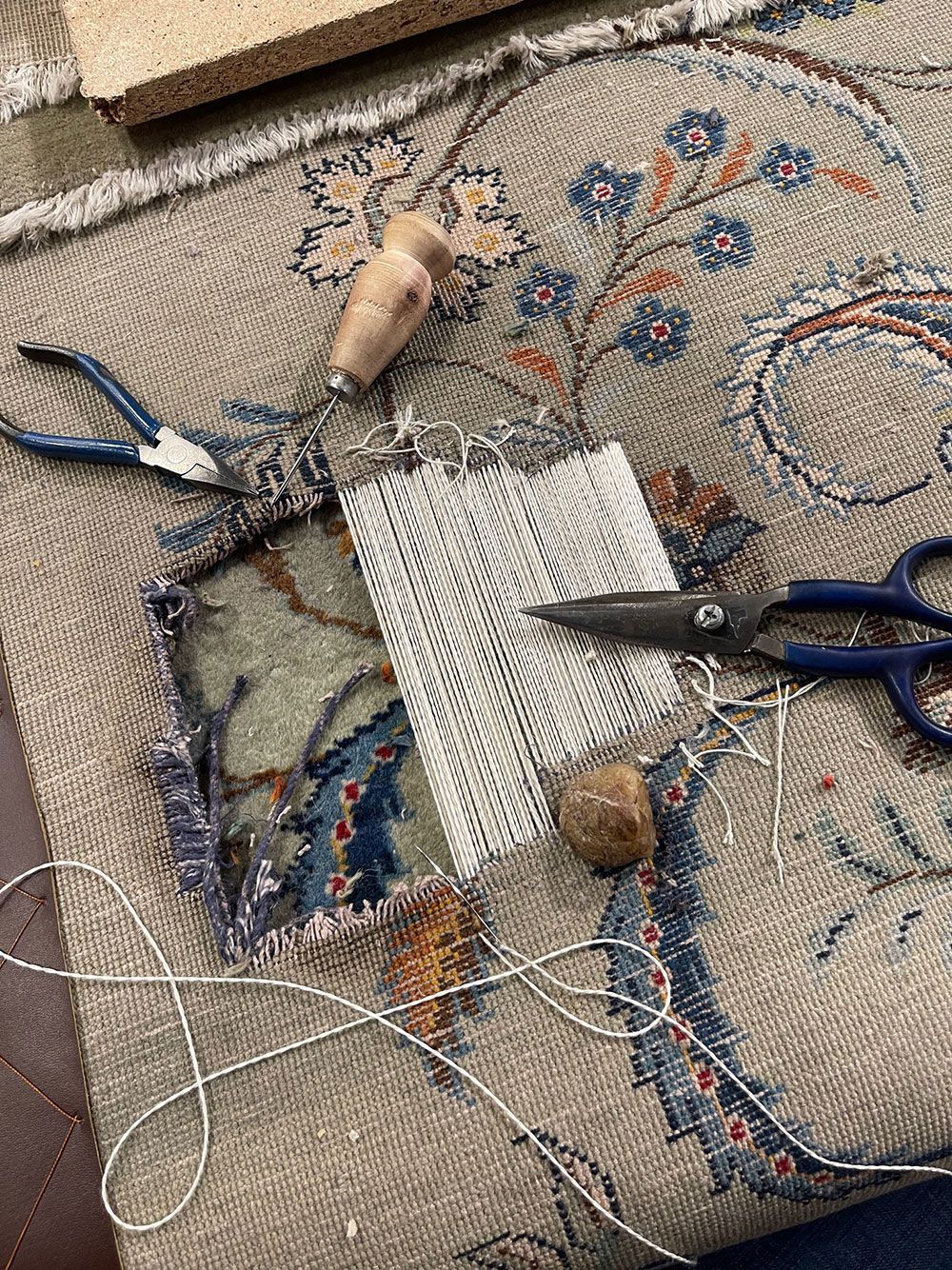 Ein Teppich wird mit Schere und Zange repariert.