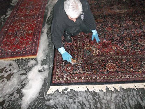 Ein Mann reinigt einen Teppich mit einer Bürste und Seife.