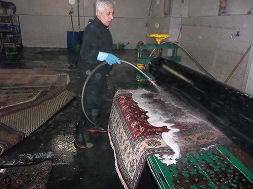 Ein Mann wäscht einen Teppich mit einem Schlauch