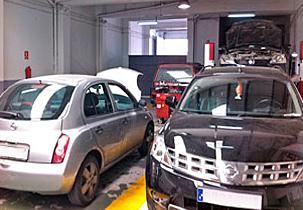 Dos coches están aparcados en un garaje con el capó abierto.