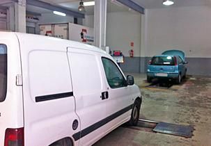 Una furgoneta blanca está aparcada en un garaje al lado de un coche azul.