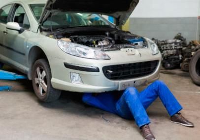 Un hombre está tendido debajo de un coche con el capó abierto.