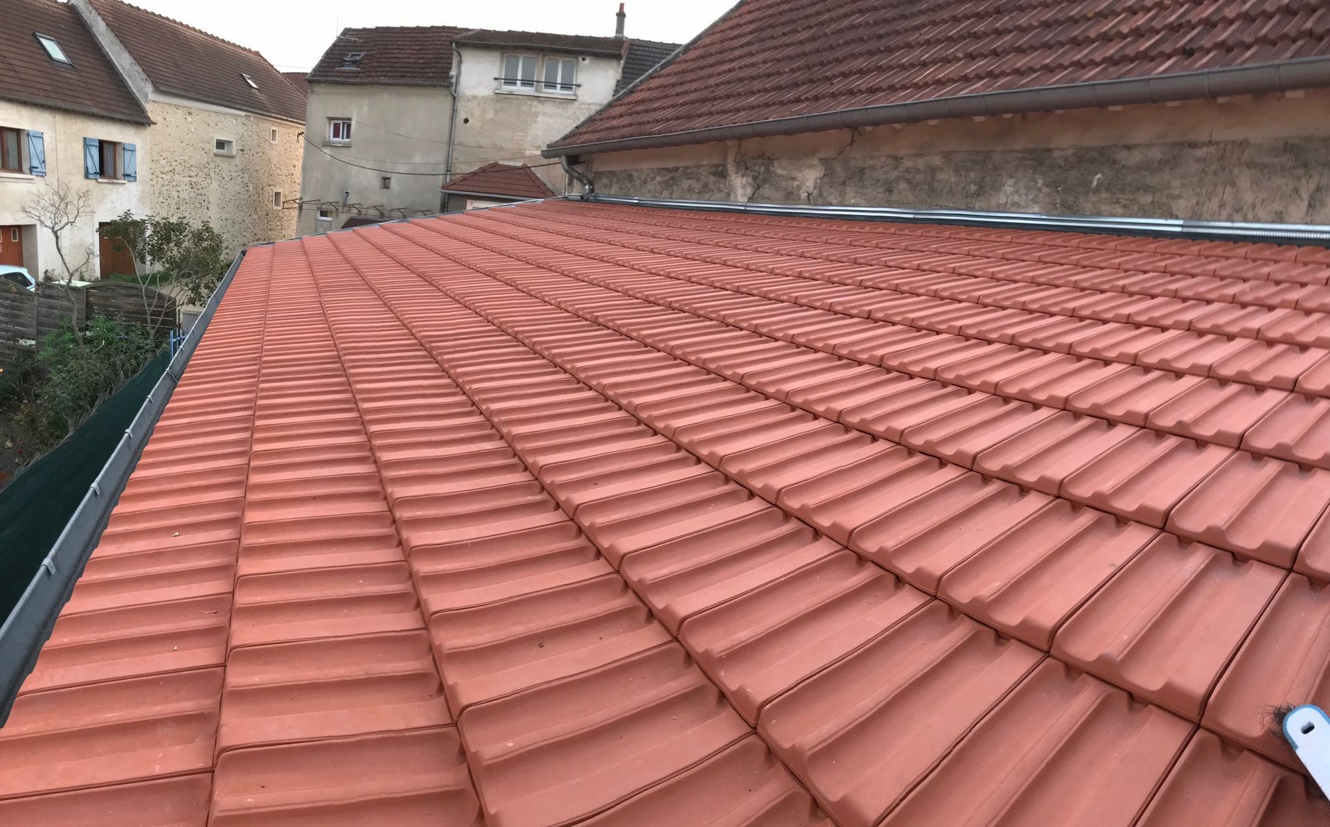 Toit de tuiles rouges sur la cour d'un immeuble, avec des maisons voisines en arrière-plan.