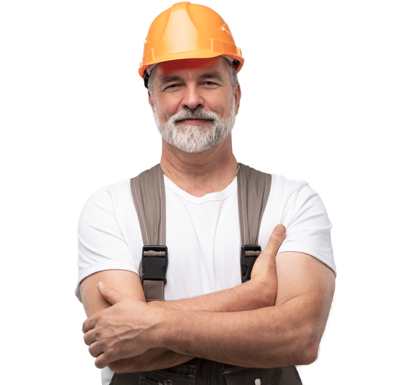 Ouvrier du bâtiment portant un casque orange, une chemise blanche et des bretelles, debout, les bras croisés.