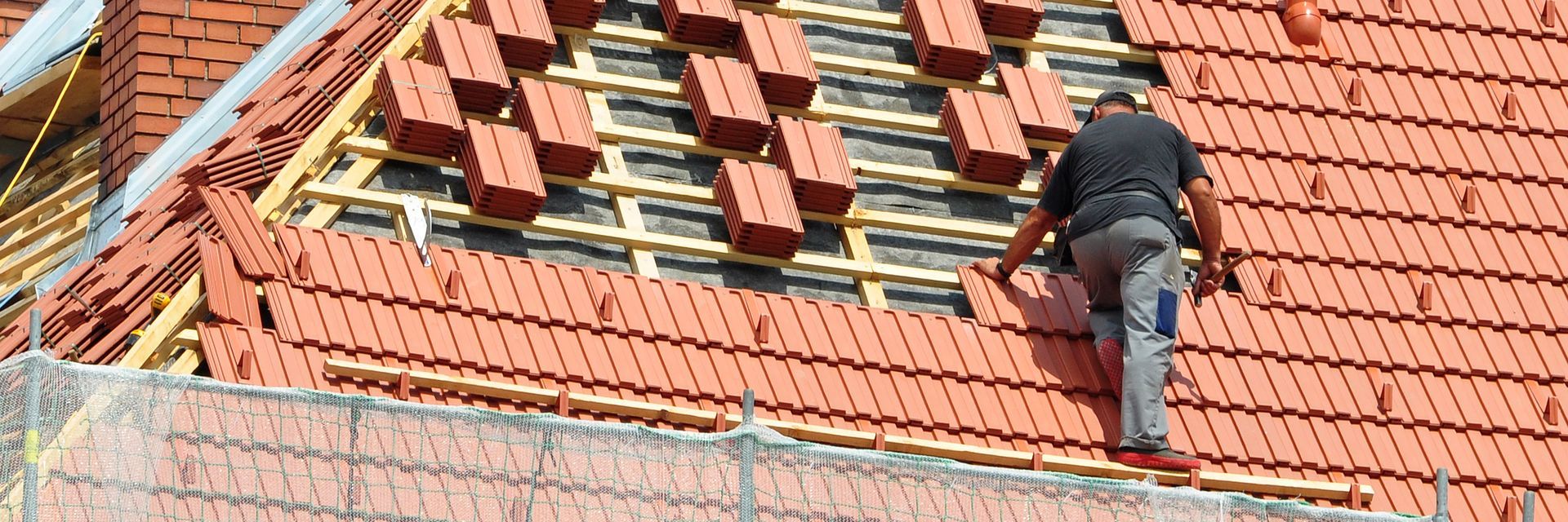 Ouvrier réparant des panneaux de toiture rouge-orangé à l'aide d'outils.