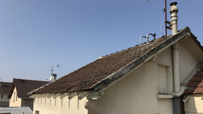 Toits de maisons beiges aux toits de tuiles brunes et à haute cheminée sous un ciel bleu clair