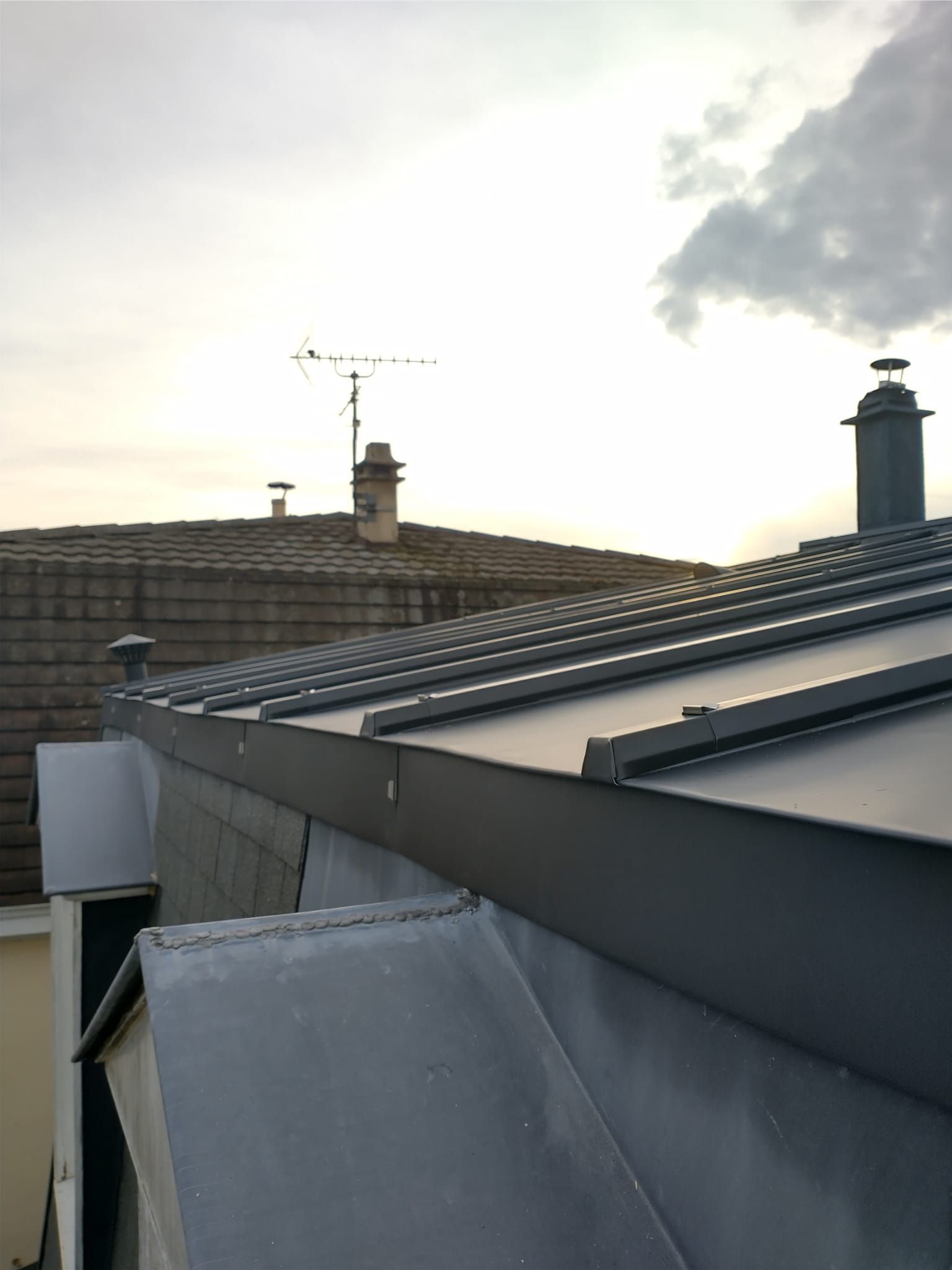 Toits au crépuscule avec panneaux solaires, cheminées et ciel nuageux
