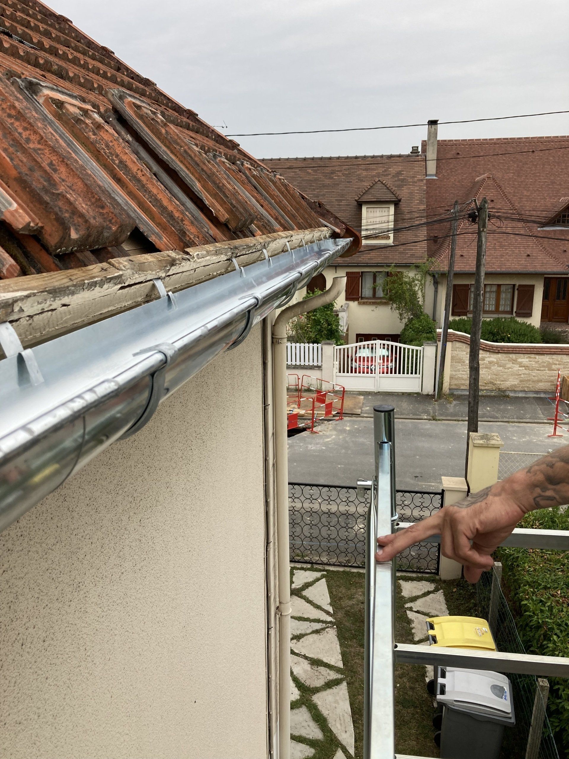 Ouvrier réparant une gouttière sur le toit d'une maison, près d'une échelle et vue de la rue